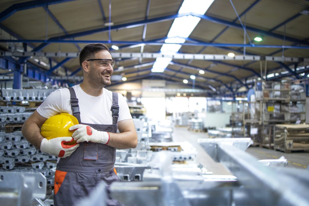 Smiling factory worker with hard hat standing in factory production line.